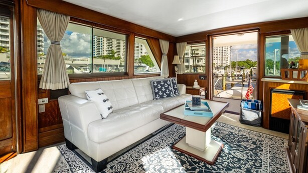 A modern interior with a sofa, coffee table, and large windows offering a marina view. - Stay Aboard a Vintage Hatteras 53' Motor Yacht in Aventura-A Unique Experience! (Aventura)