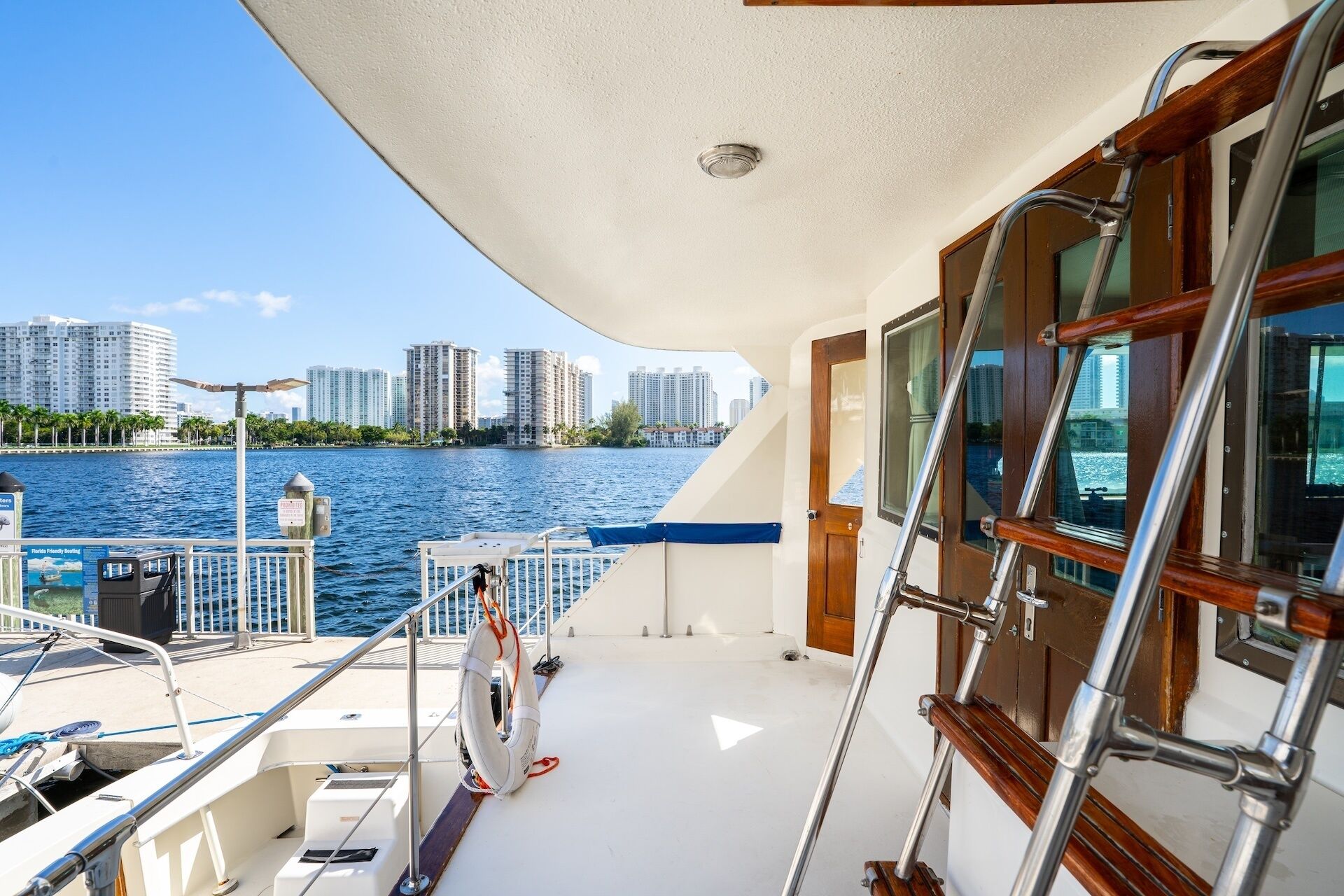 A boat deck with a view of a city skyline, a lifebuoy, and a ladder.