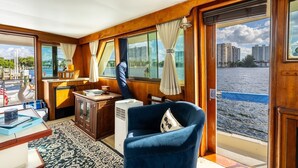 A cabin with a view of the water, a desk, a chair, and a small table with a tray. - Stay Aboard a Vintage Hatteras 53' Motor Yacht in Aventura-A Unique Experience! (Aventura)