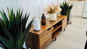 Ein Konsolentisch aus Holz mit einer weißen Lampe, einer Vase mit getrockneten Blumen und einer Topfpflanze.