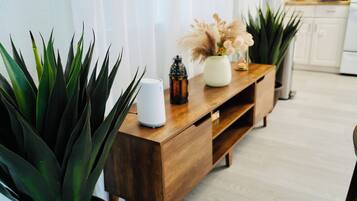 Una consola de madera con una lámpara blanca, un jarrón con flores secas y una planta en maceta.