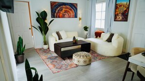 Ein Wohnzimmer mit Sofa, Couchtisch, Hocker und Topfpflanzen.