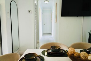 A dining area with a table set for two, a television mounted on the wall, and a hallway leading to a door. - Hollywood 7881 (Hollywood)