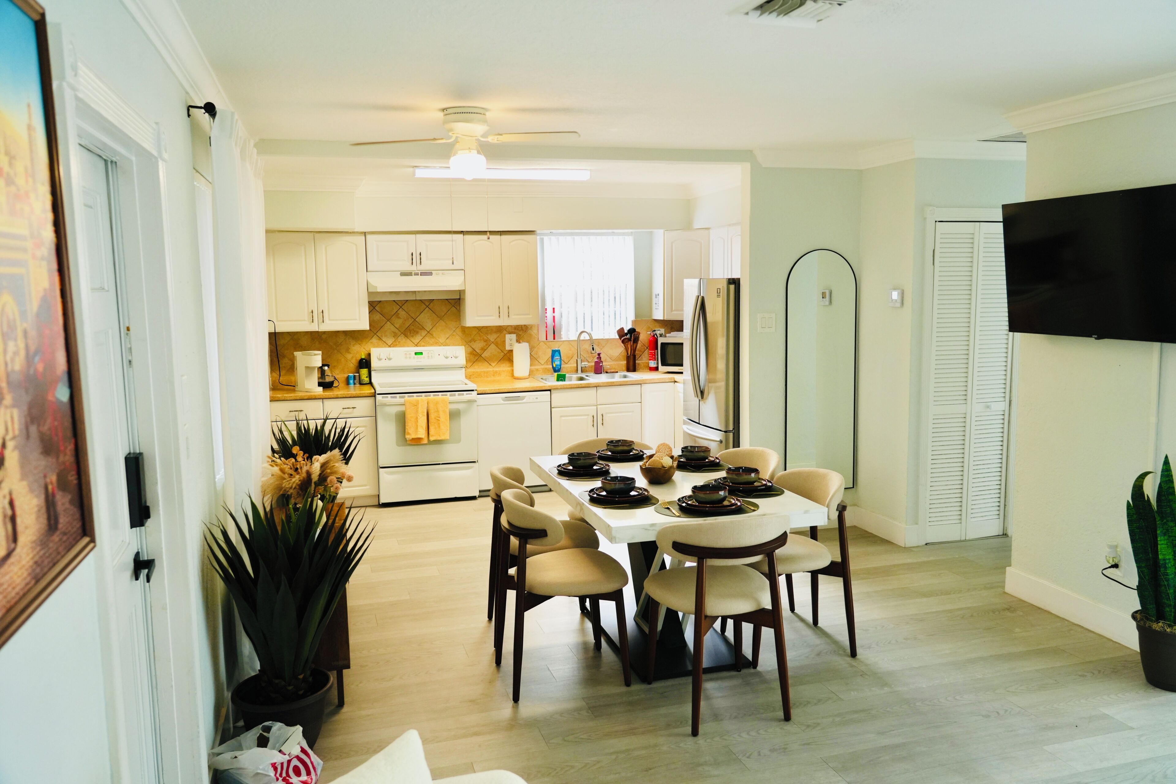Una cocina moderna con armarios blancos, una mesa de comedor con sillas, un refrigerador y un televisor de pantalla plana montado en la pared.