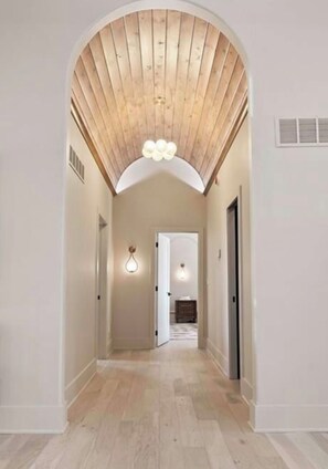 A hallway with an arched ceiling, wooden floor, and a light fixture. - Spacious Leawood Retreat 4BR • 5BA • Sleeps 10+ • Basement Bar (Leawood)