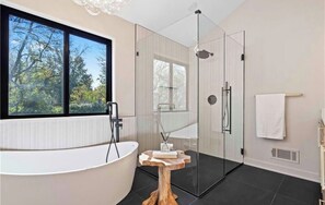 A modern bathroom with a bathtub, glass shower enclosure, and a window with a view of trees. - Spacious Leawood Retreat 4BR • 5BA • Sleeps 10+ • Basement Bar (Leawood)