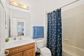 Ein Badezimmer mit weißem Waschbecken, einem Spiegel, einer Toilette, einem blauen Handtuch und einer Duschvorhang.