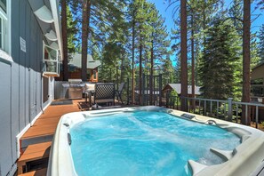 Een hottub op een houten terras, met uitzicht op een bos en een chalet.