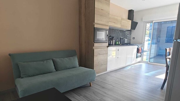 A modern living room with a sofa, a coffee table, and a kitchen area with a microwave and cabinets. - Apartment near Dune du Pilat (La Teste-de-Buch)