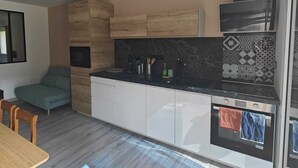 A modern kitchen with a dining area, wooden cabinets, a black countertop, and a built-in oven. - Apartment near Dune du Pilat (La Teste-de-Buch)