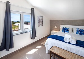 Ein Schlafzimmer mit Bett, Nachttisch, Fenster mit Vorhängen, Blick ins Freie und einer Wandlampe.