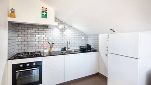 Ett kök med vita skåp, en svart bänkskiva, en spis, en ugn och ett kylskåp.