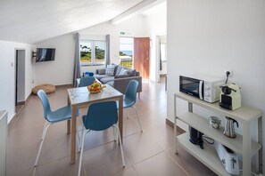 Ein modernes Zimmer mit Esstisch, Stühlen, einer Couch, einem Fernseher und einer Küchenzeile mit Geräten.