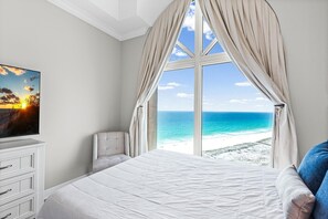 Ein Schlafzimmer mit großem Fenster, einem Bett, einem Sessel und einem Fernseher.