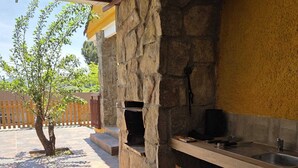 An outdoor kitchen area with a stone wall, a wooden counter, and a bag of charcoal.