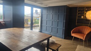 A room with a wooden table, a blue door, a bookshelf, and a view of the outside.
