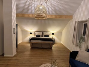 Ett sovrum med en säng, sänglampor, en hängande taklampa och ett fönster med gardiner.