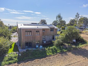 A modern two-story house with a flat roof, large windows, and a visible outdoor seating area.