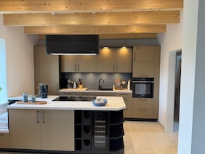 A modern kitchen with built-in appliances, a large island, and a wooden ceiling.