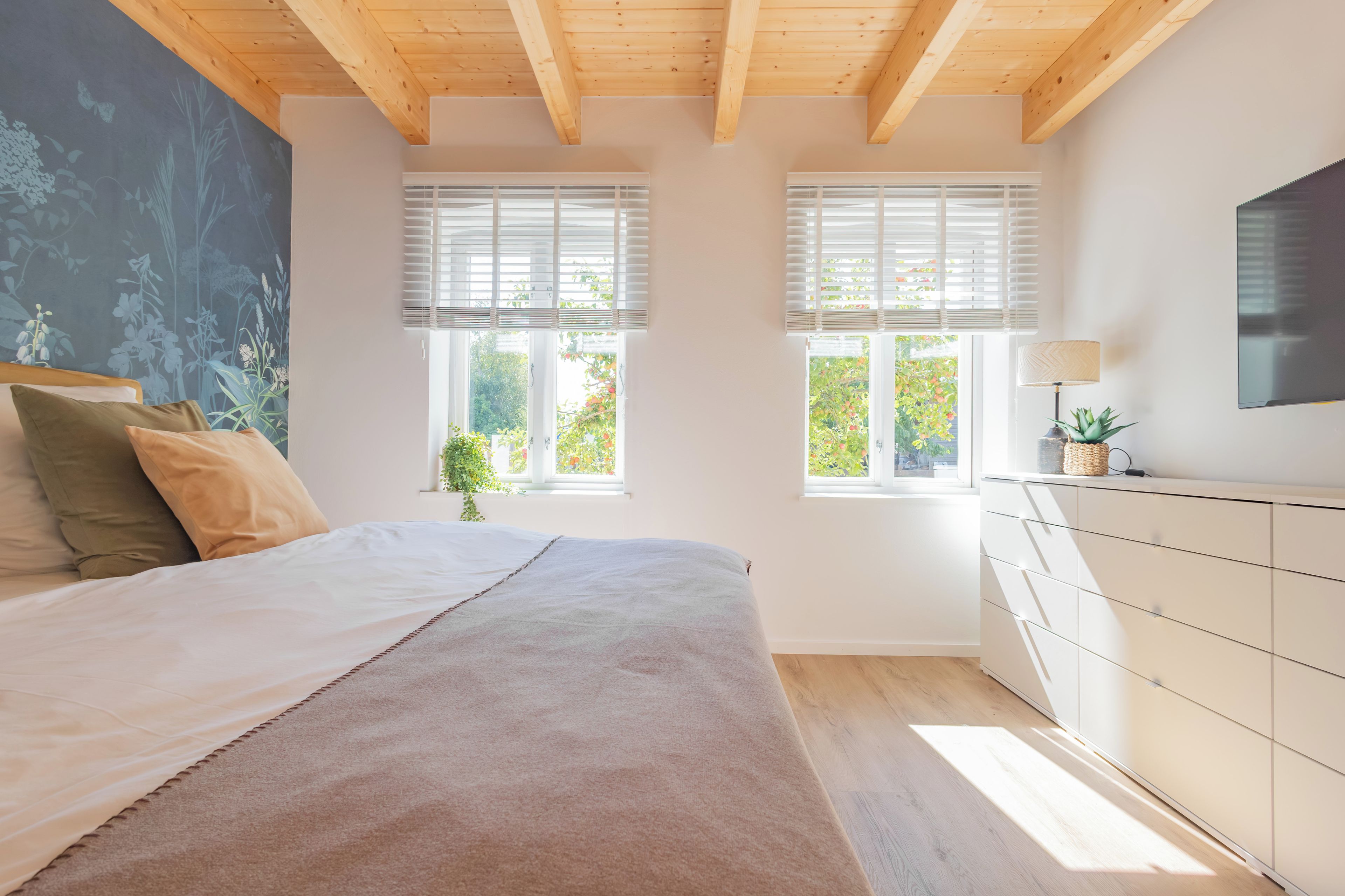 A bedroom with a bed, a dresser, two windows, and a wall with a botanical mural.