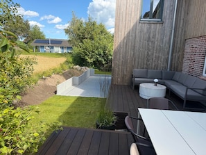 Un patio moderno al aire libre con un sofá integrado, una mesa redonda y una pequeña zona ajardinada con césped y un muro de ladrillo.