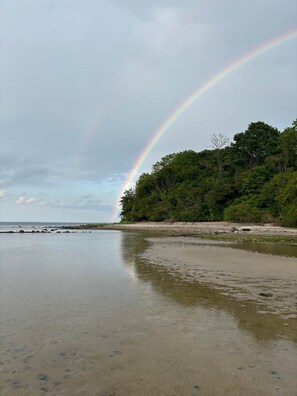 A beach with a rainbow, calm water, and a forested area. - Die Alte Meierei (Steinbergkirche)