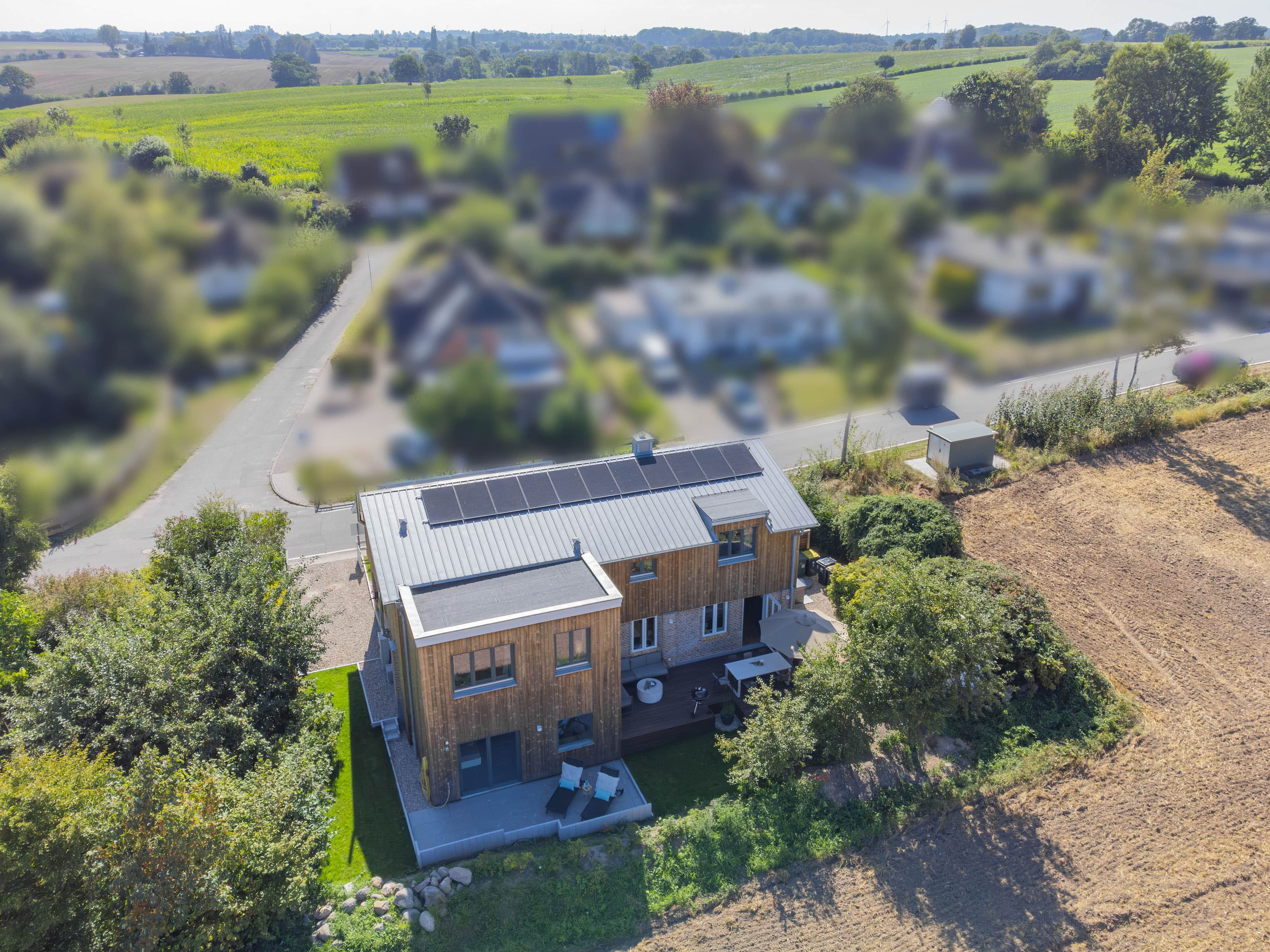 A modern two-story house with a flat roof, solar panels, and a small garden area.