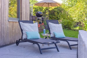 Two lounge chairs with cushions, a barbecue grill, and a table with a glass and book.