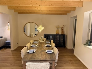 A dining area with a wooden table set for six, a large mirror, and a hanging light fixture.