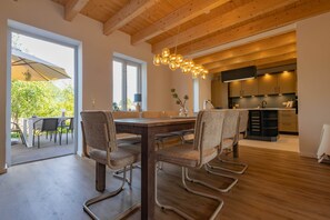 Ein moderner Essbereich mit Holztisch und Stühlen, eine Küche inklusive Fernseher und Blick ins Grüne.