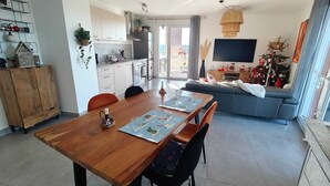 Une cuisine moderne avec des meubles blancs, une table à manger avec des sets de table, un canapé bleu et un téléviseur fixé au mur.