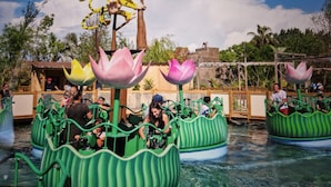Une attraction aquatique avec des bateaux verts et de grandes décorations en forme de lotus roses.