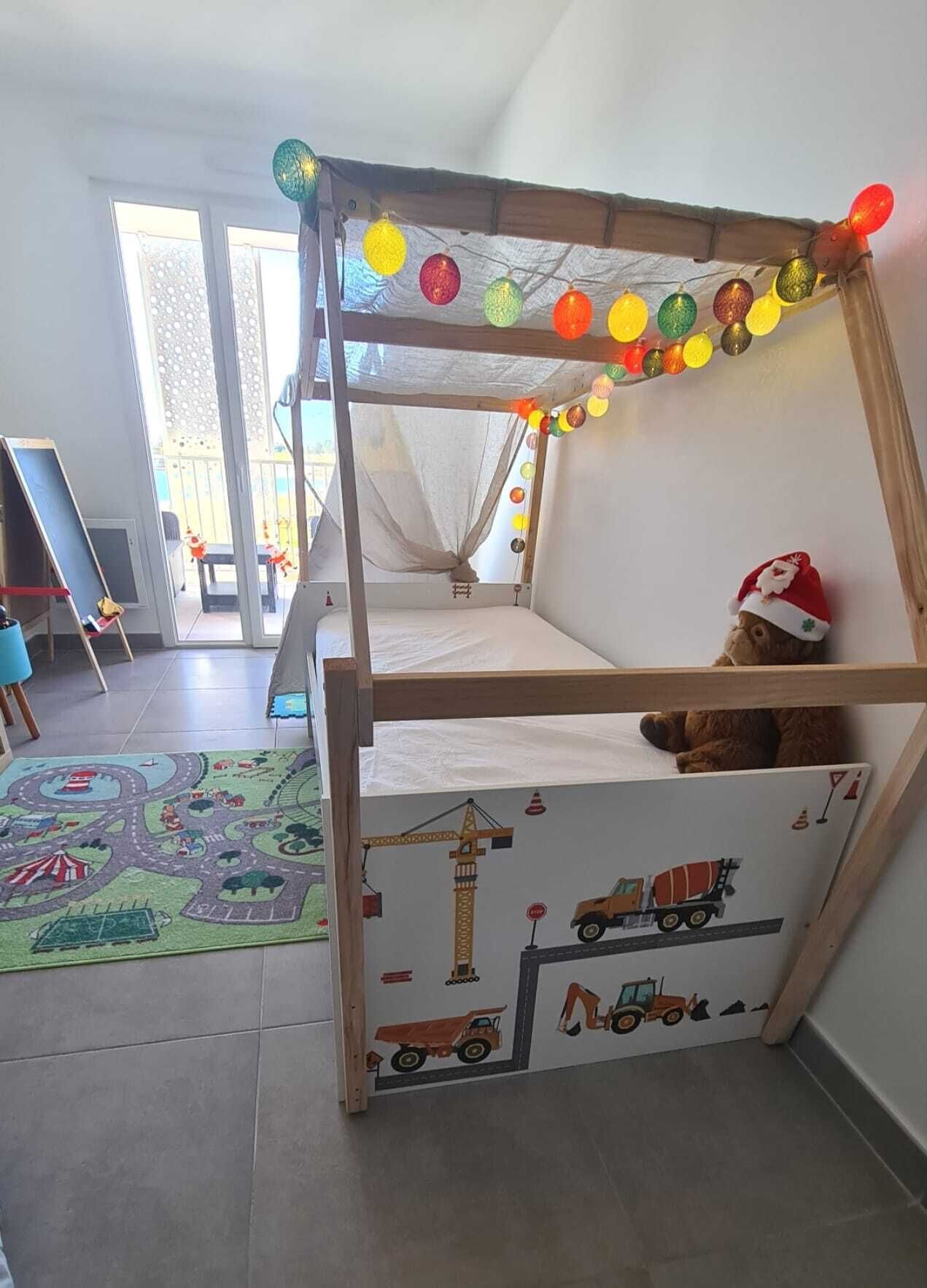 Un lit superpos é pour enfant avec un matelas aux motifs de chantier de construction, un ours en peluche et des lumières colorées.