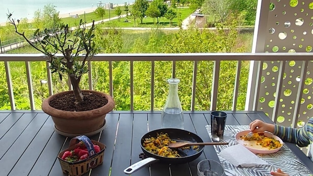 Un balcon avec une table dressée pour deux personnes, un pot de fleurs, une bouteille et un saladier rempli de fraises.