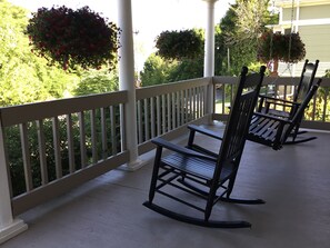 Eine Veranda mit zwei Schaukelstühlen, weißen Geländern und Blumenkörben.