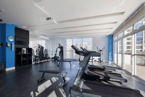 Une salle de sport moderne équipée de tapis de course, de machines de musculation et offrant une vue sur la ville.