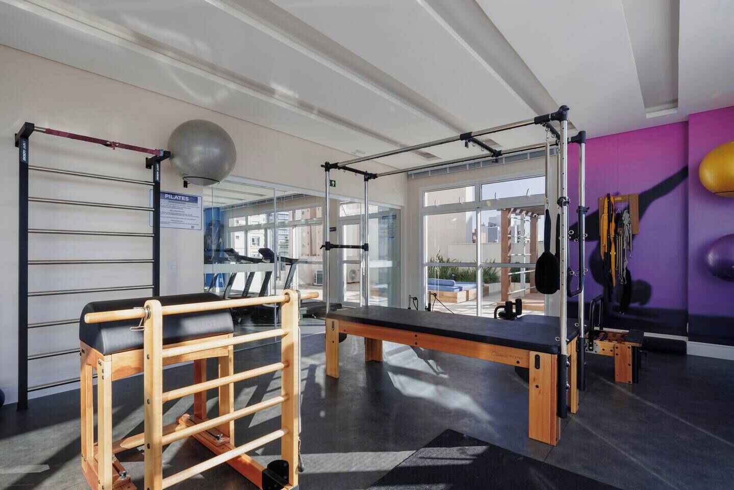 A gym with exercise equipment, a Pilates area, and large windows.