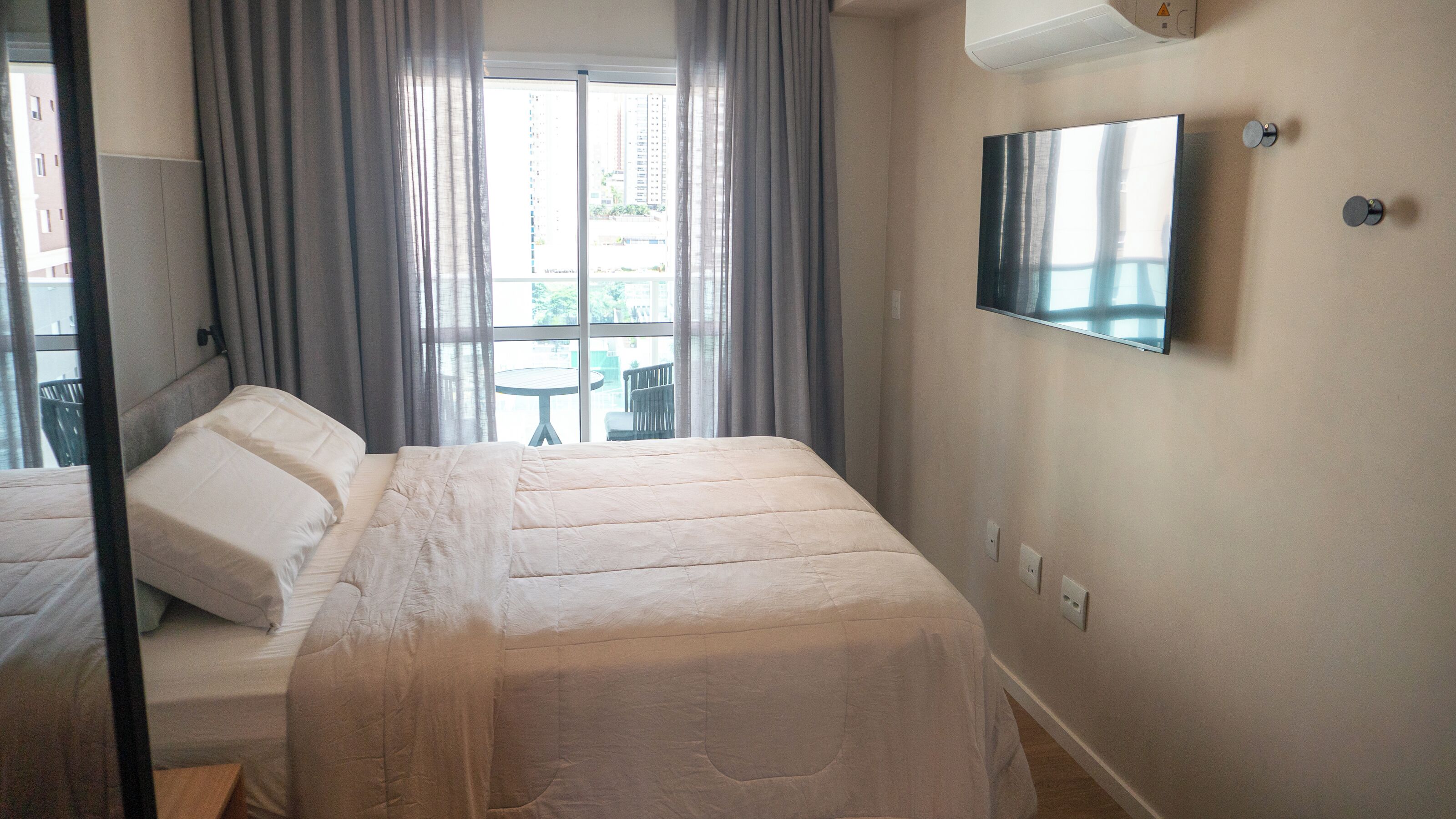 A hotel room with a bed, a TV mounted on the wall, and a window with curtains.
