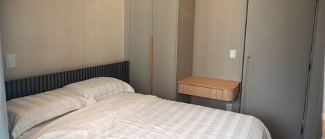 A bedroom with a bed, a bedside table, a wardrobe, and a wall-mounted light switch.
