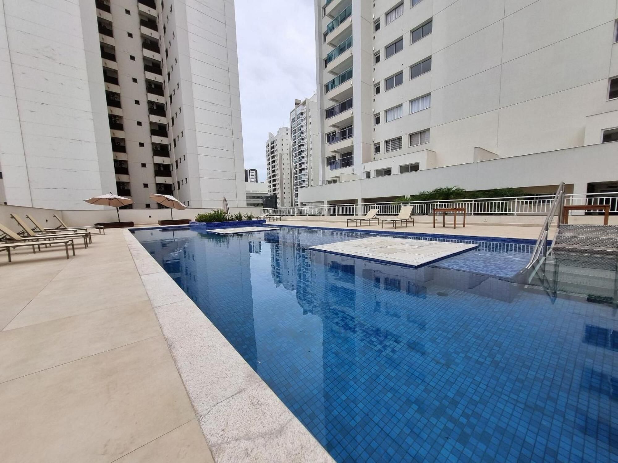 A swimming pool with lounge chairs and umbrellas, surrounded by high-rise residential buildings.. Best of Palhano - 1 Suite + 1 Bedroom