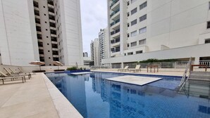 Una piscina amb gandules i ombrel·les, envoltada d'edificis residencials alts.