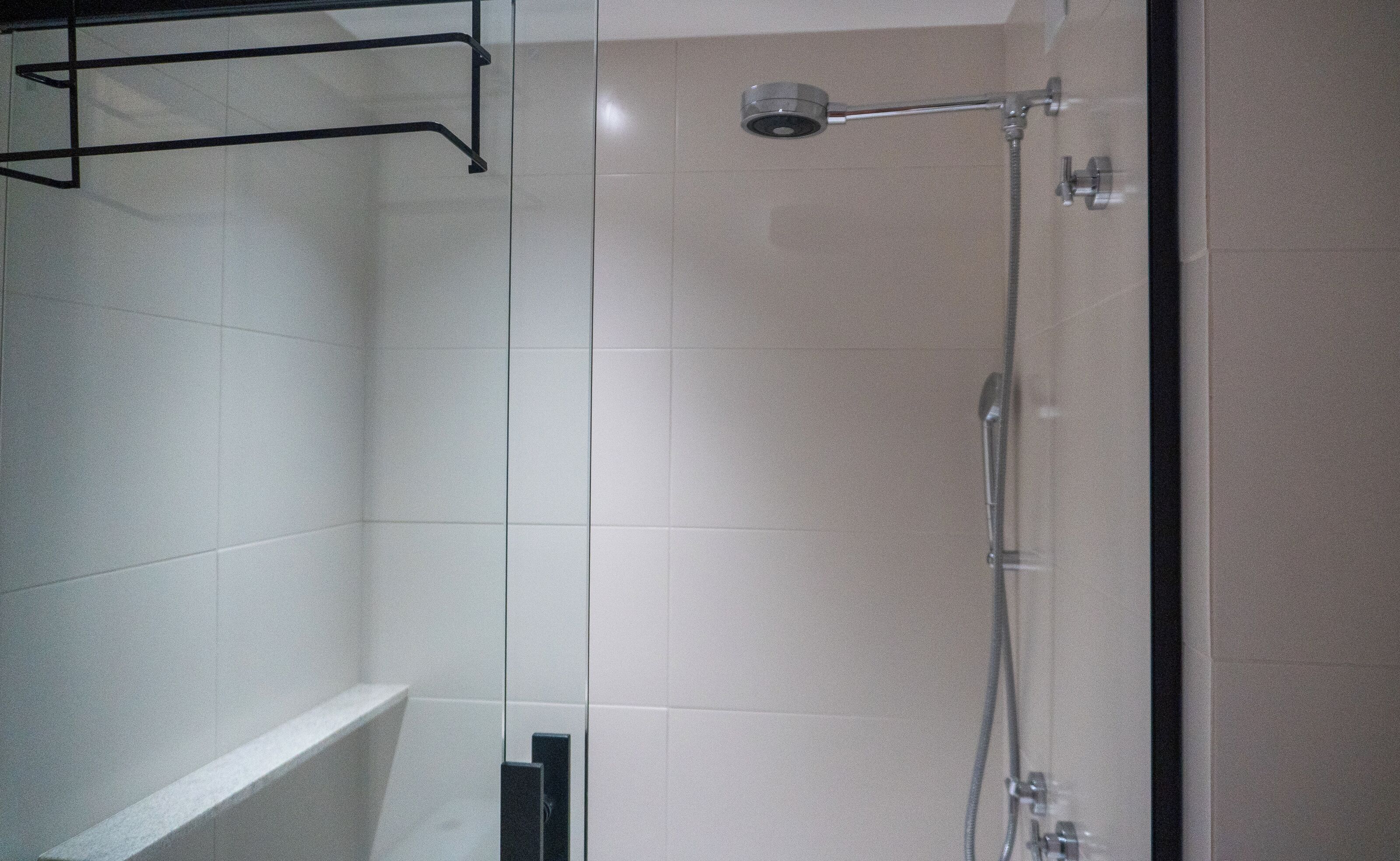 Una ducha con cabezal de ducha de mano, un perchero en la pared y suelo de baldosas.