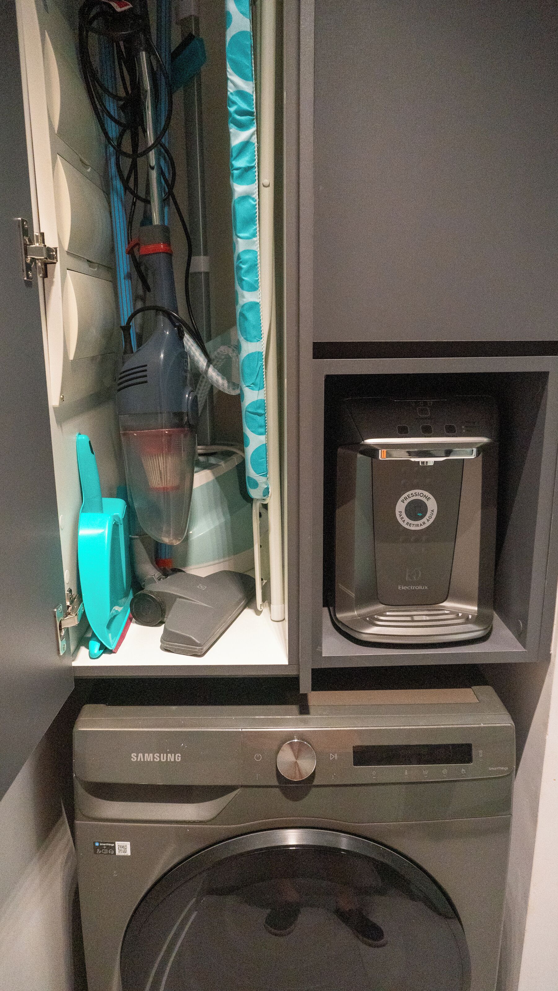 A washing machine, a vacuum cleaner, and a microwave in a compact kitchen area.
