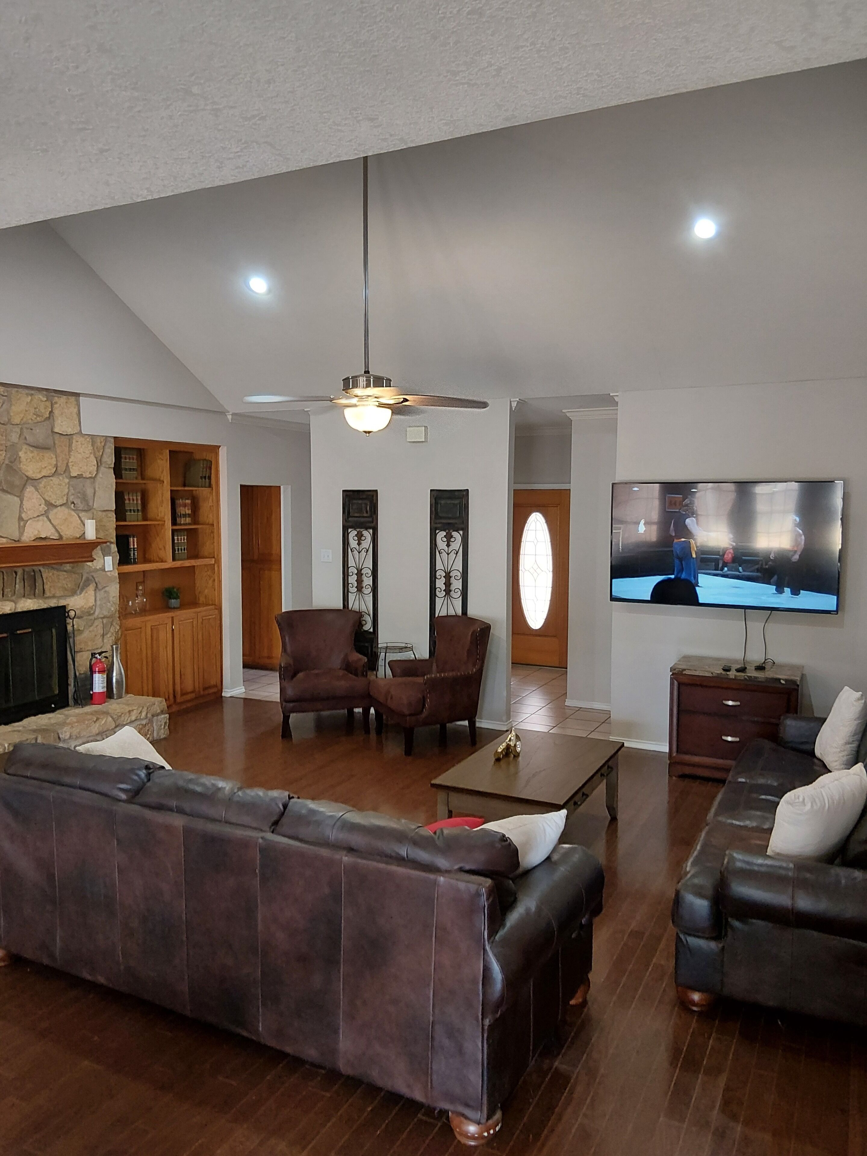 A living room with a stone fireplace, leather sofas, a television, and a ceiling fan.