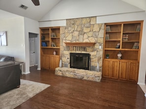 Una sala de estar con chimenea de piedra, estanterías de madera con libros y un sofá gris.