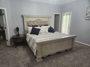 Un dormitorio con una cama grande, una mesita de noche, una lámpara y una puerta.
