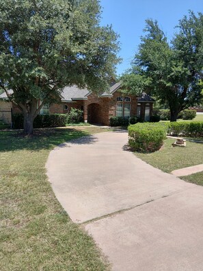 A residential house with a brick exterior, a driveway, and a well-maintained lawn.