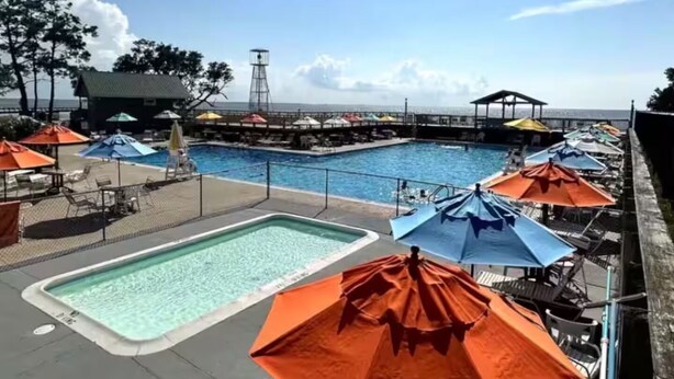 A pool area with multiple umbrellas, lounge chairs, and a view of the ocean. - Lily's Pad (Kill Devil Hills)