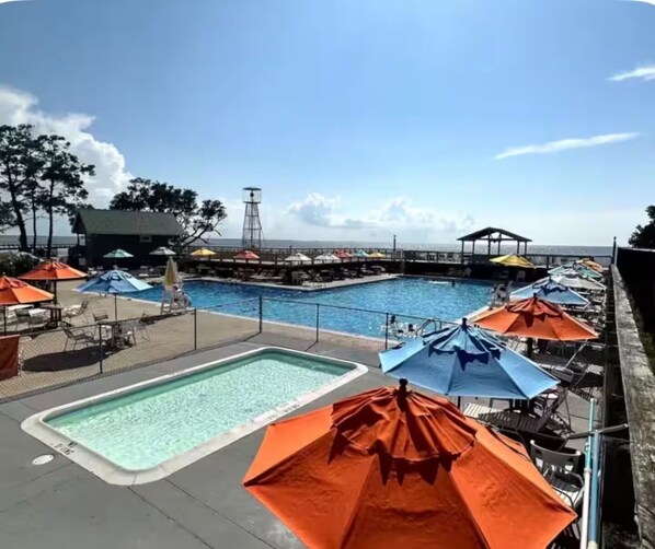 A pool area with multiple umbrellas, lounge chairs, and a view of the ocean.