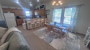A kitchen with wooden cabinets, a refrigerator, a sink, and a dining area with a table and chairs. - Lily's Pad (Kill Devil Hills)